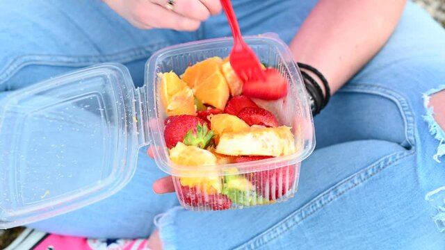 Close-up of a woman's hands opening a tupper with fruit to eat