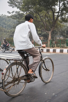 Bicyclist on old bike on the streets photographed from behind. White shirt and dark hair. Indian. Left an motorcycle.  Normal perspective. 
