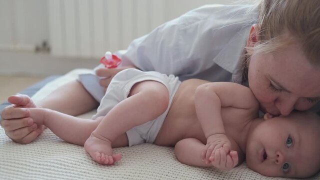 4k. Attractive happy mother kiss lying with little baby boy. Happy family