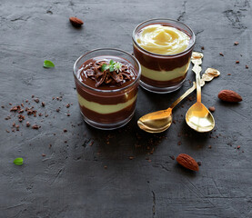 Vegan pudding. Chocolate and vanilla pudding in glasses with almonds and spoons on a black background with space for text. Top view