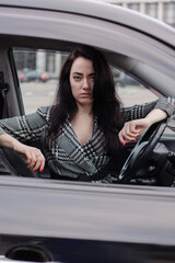 Fototapeta na wymiar portrait of attractive brunette in grey checkered dress in a black car. girl in automobile. business woman