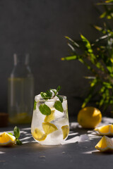 Lemonade with lemon, mint and ice cubes in glass on gray stone background.
