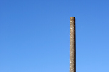 A simple concrete post. A long pole under a blue sky on a sunny day. Loneliness and minimalism.