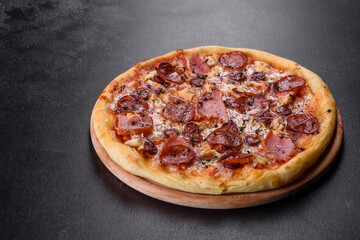 Delicious fresh oven pizza with tomatoes, salami and bacon on a dark concrete background