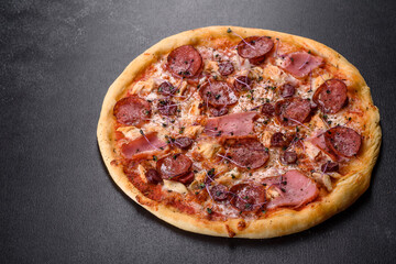 Delicious fresh oven pizza with tomatoes, salami and bacon on a dark concrete background