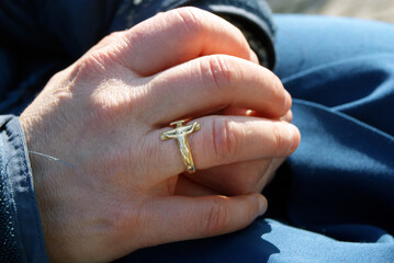 Nun's hands with ring in the shape of a crucifix.
Faithful woman prays outdoors under the sun.