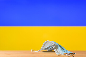 A medical mask lies on the table against the background of the flag of Ukraine. The concept of a...