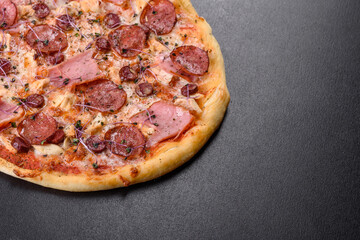 Delicious fresh oven pizza with tomatoes, salami and bacon on a dark concrete background