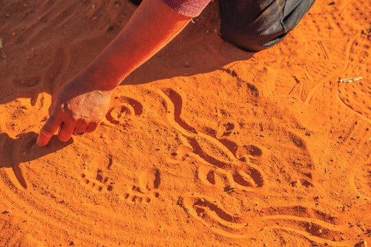 aboriginal woman hands creating shapes with red sand on the ground in aboriginal art style. Northern Territory, Australia