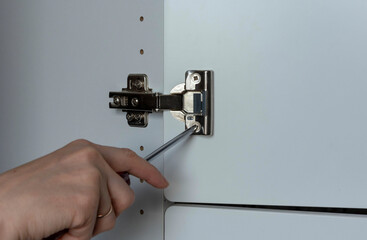 adjusting the furniture hinge of the home cabinet door with a screwdriver, hand with a screwdriver...