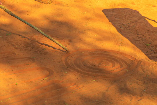 Aboriginal People Creating Shapes With Red Sand On The Ground In Aboriginal Art Style. Northern Territory, Australia