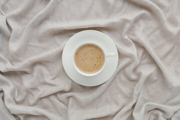 Cup of coffee with milk on the bed with grey linen bed sheet. Morning coffee concept. Sunday loneliness relaxing, hugge mood. Minimalism composition with pastel neutral colors. Top view