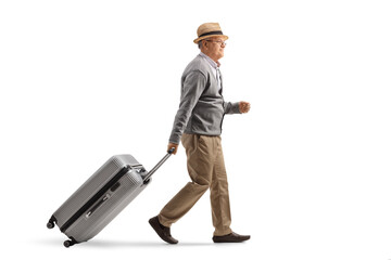 Full length profile shot of an elderly man walking and pulling a suitcase
