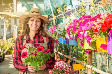 Foto op Canvas Happy young female smiling florist in a greenhouse in garden center with red flowers © BigDreamStudio
