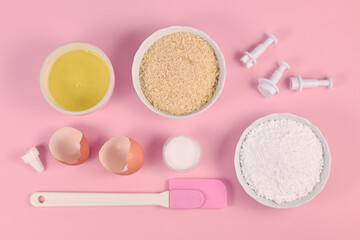 Ingredients for making homemade French Macarons sweets including powdered sugar, ground almonds, egg white, salt and baking tools on pink background