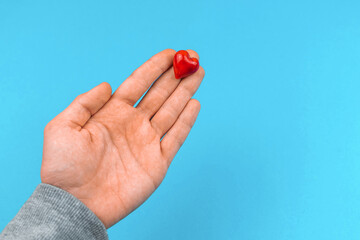 Young man hand gives a small red heart, help and donate concept background