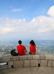 A boy and a girl (young couple) admire the mountain landscape, sitting on the parapet of the observation deck.