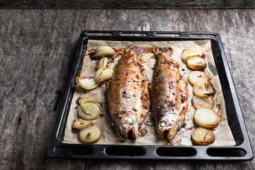 Baked rainbow trout with onion and spices on baking tray on wooden table