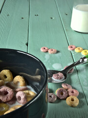 Primer plano de un bol negro con cereales de colores sobre una mesa de madera verde claro en la que...