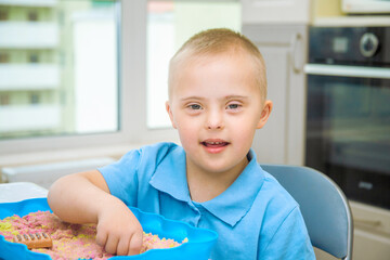 Portrait of a cute boy with Down syndrome, a child playing with sand and molds for modeling, early...
