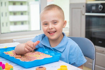 Portrait of a cute boy with Down syndrome, a child playing with sand and molds for modeling, early...