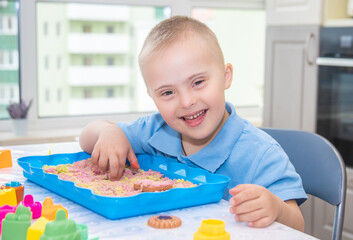 Portrait of a cute boy with Down syndrome, a child playing with sand and molds for modeling, early...