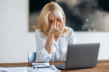Tired upset Caucasian mature blonde, ceo, manager or freelancer, in white shirt, tired of online...