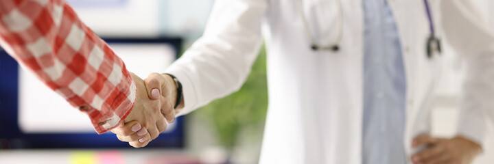 Doctor with stethoscope around neck shaking patients hand in clinic closeup