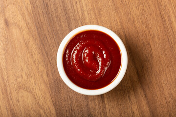 Tomato ketchup in the ramekin on wooden background.