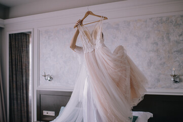 morning of the bride, getting ready, the bride in a robe holds a wedding dress hanging on a hanger