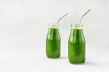 Green smoothie with spinach in two small bottles with metal straw on a light background. Healthy lifestyle concept.