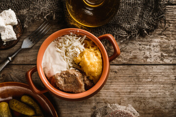 Fototapeta na wymiar Delicious polenta with meat, cheese and sour cream in the bowl on rustic wooden background. Traditional romanian food, top view