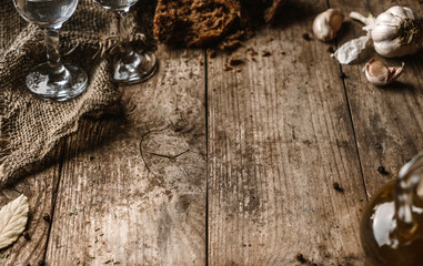 Wooden table with empty space in the center frame, selective focus. Glasses of vodka, bread, napkin and spices on rustic background, cooking, close up