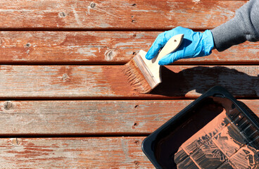 Gloved hand applying stain on home cedar wooden deck boards