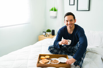 Attractive man enjoying breakfast in bed