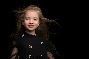 A beautiful little girl stands in the wind, her hair and clothes
