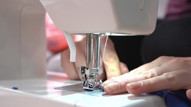 Skilled seamstress overcasts edge of blue serge fabric with contemporary sewing machine at workplace in room extreme closeup
