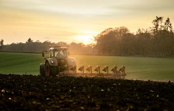 Ploughing a field at sunset with a tractor and plough, ready for crops on a farm