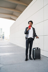 Tourist man using his mobile phone and carrying suitcase outdoors.