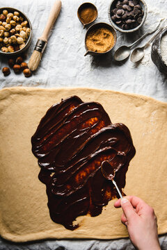 Spreading the chocolate on the dough with hand in motion  and ingredients arranged on the table cloth pictured from above