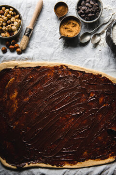 Chocolate spread on the dough and ingredients arranged on the table cloth pictured from above