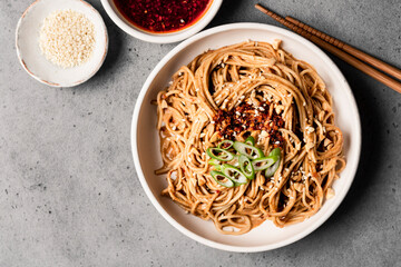Spicy sesame noodles in a bowl next to chile oil and sesame seeds.