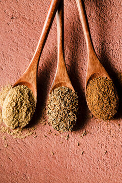 Three wooden spoons holding dired corriandor, cumin seed, and chipotle chile powder.