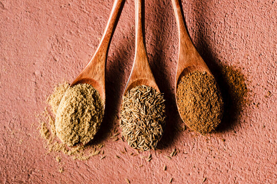 Three wooden spoons holding dired corriandor, cumin seed, and chipotle chile powder.