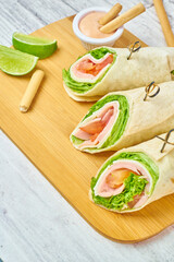 Light breakfast of three ham and cheese wraps on wooden board with healthy orange juice