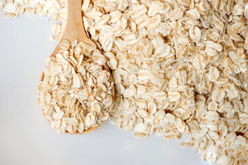 Close-up rolled oats in a wooden cup and spoon on white background is a healthy whole grain food.