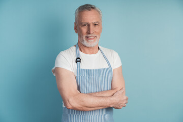 Attractive, elderly man in a blue apron posing on a blue background. Handsome man isolated on blank wall background