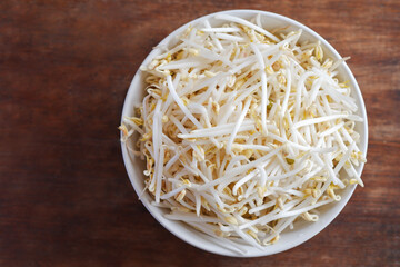 Bean sprouts in a white ceramic cup placed on a brown wooden table, the view from the top.