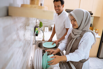 happy muslim young couple wash the dishes after having iftar dinner together in the kitchen sink