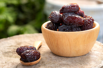 Large date palms (medjool) in cups and wooden spoons with blurred natural background.